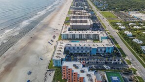 An aerial view of a coastal hotel with multiple buildings, a beach, and a parking lot. - Top Floor Beauty with Amazing Views of Beach and Pool (New Smyrna Beach)
