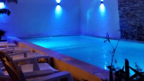 Zona de piscina con iluminación azul ambiental, sillas de descanso y palmeras.