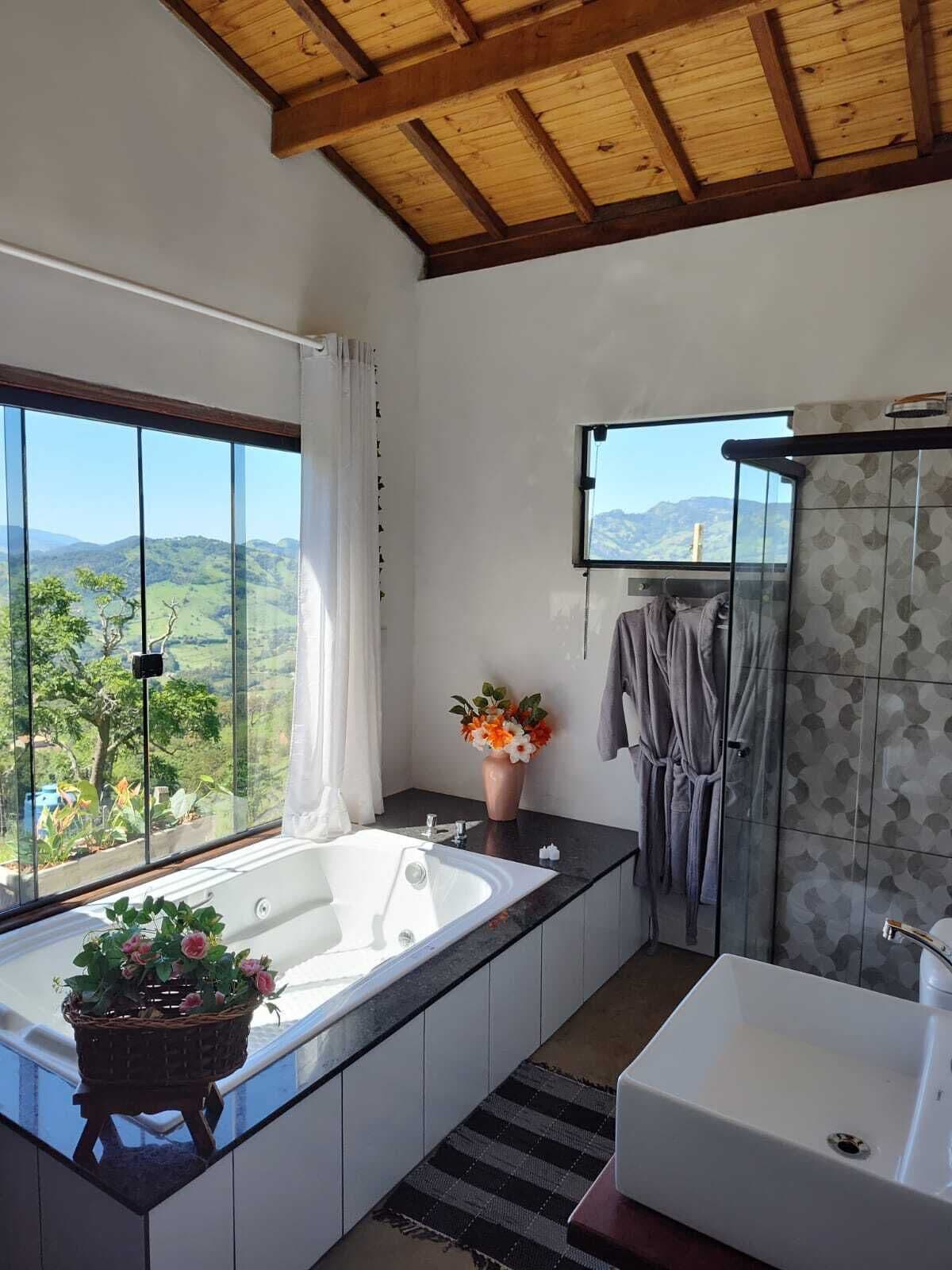 A modern bathroom with a large bathtub, a shower, and a sink. There is a window with a view of a green landscape.