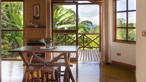 A wooden dining table with benches, a potted plant, and a view of lush greenery through large windows. - Pousada Vitória (Gonçalves)