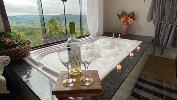 A modern kitchen with a large window, a wooden countertop, and a view of the countryside. - Pousada Vitória (Gonçalves)