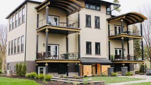 A modern two-story house with a balcony on each floor, a front porch, and a landscaped yard. - The Hemlock Loft (Boyne City)