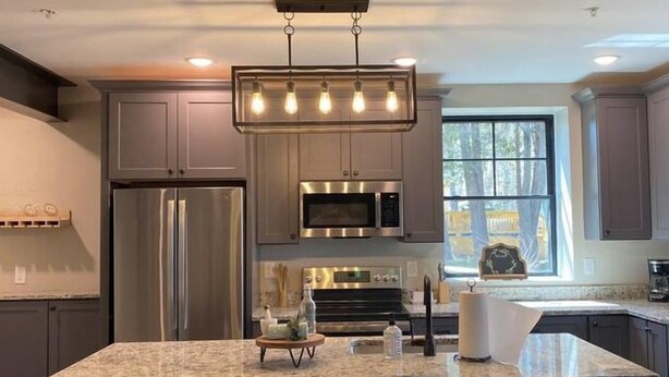 A modern kitchen with a large island, stainless steel appliances, and bar stools. - The Hemlock Loft (Boyne City)