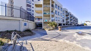 A multi-story residential building with balconies, a gated entrance, and a clear sky. - Ocean Views, Balcony, Pool, STEPS to Beach, Restaurants, Shops (Wrightsville Beach)