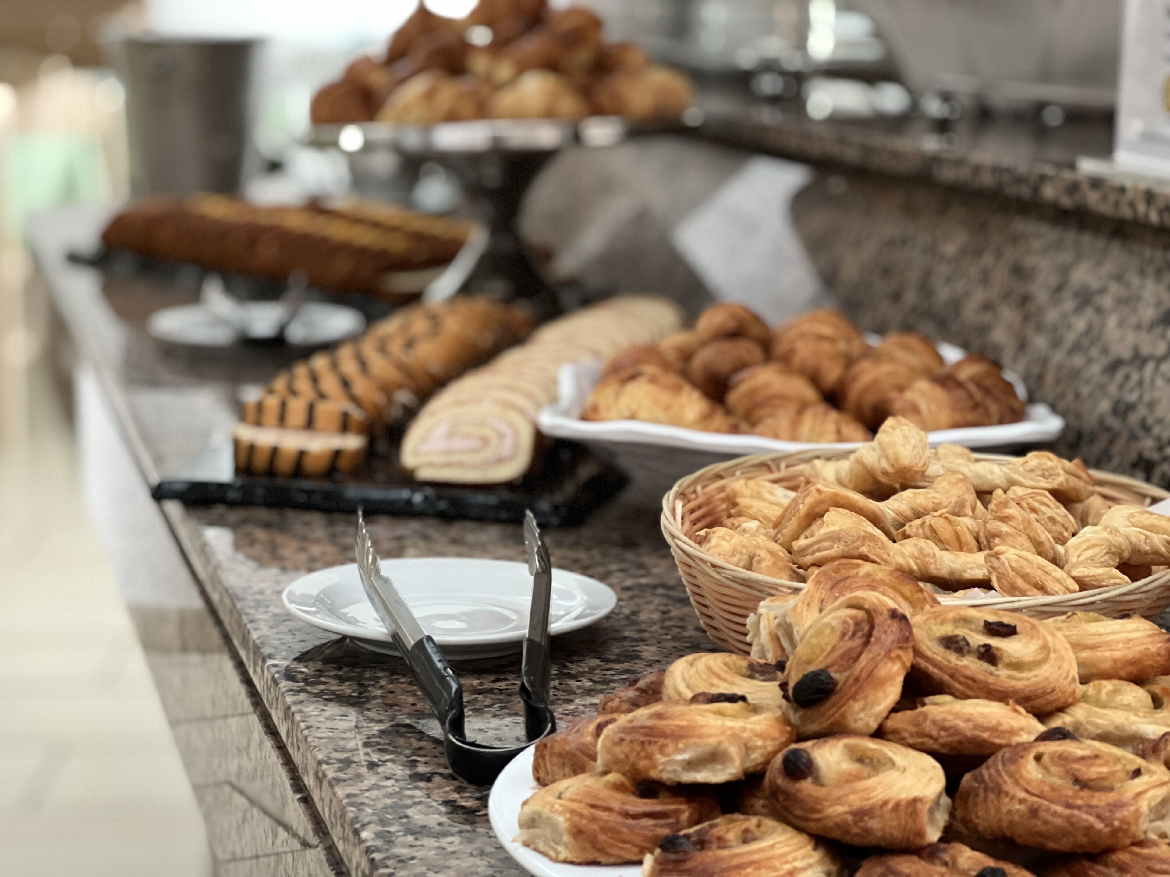 Un buffet proposant une variété de viennoiseries et de pains, notamment des croissants et des petits pains, disposés sur un comptoir en marbre.