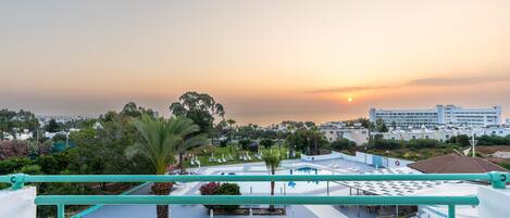 Vue depuis le toit d’un hôtel, avec une piscine, de la verdure et un coucher de soleil en arrière-plan.