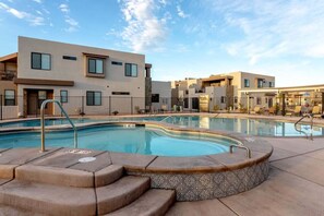 A modern hotel with a swimming pool, outdoor seating, and a clear sky.