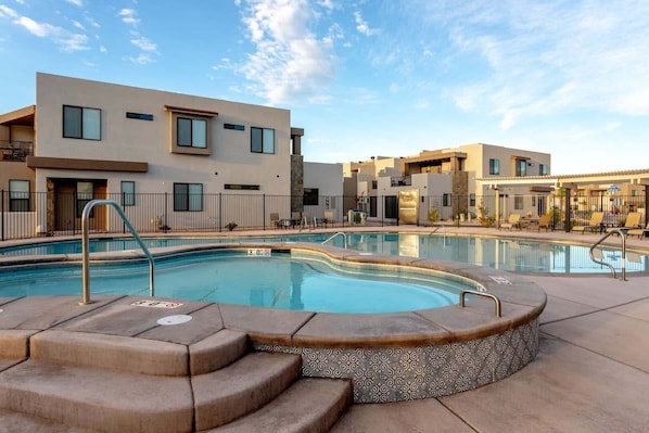 A modern hotel with a swimming pool, outdoor seating, and a clear sky.