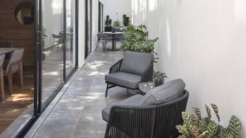A modern interior with a glass door leading to a dining area, a seating area with a table and chairs, and potted plants.