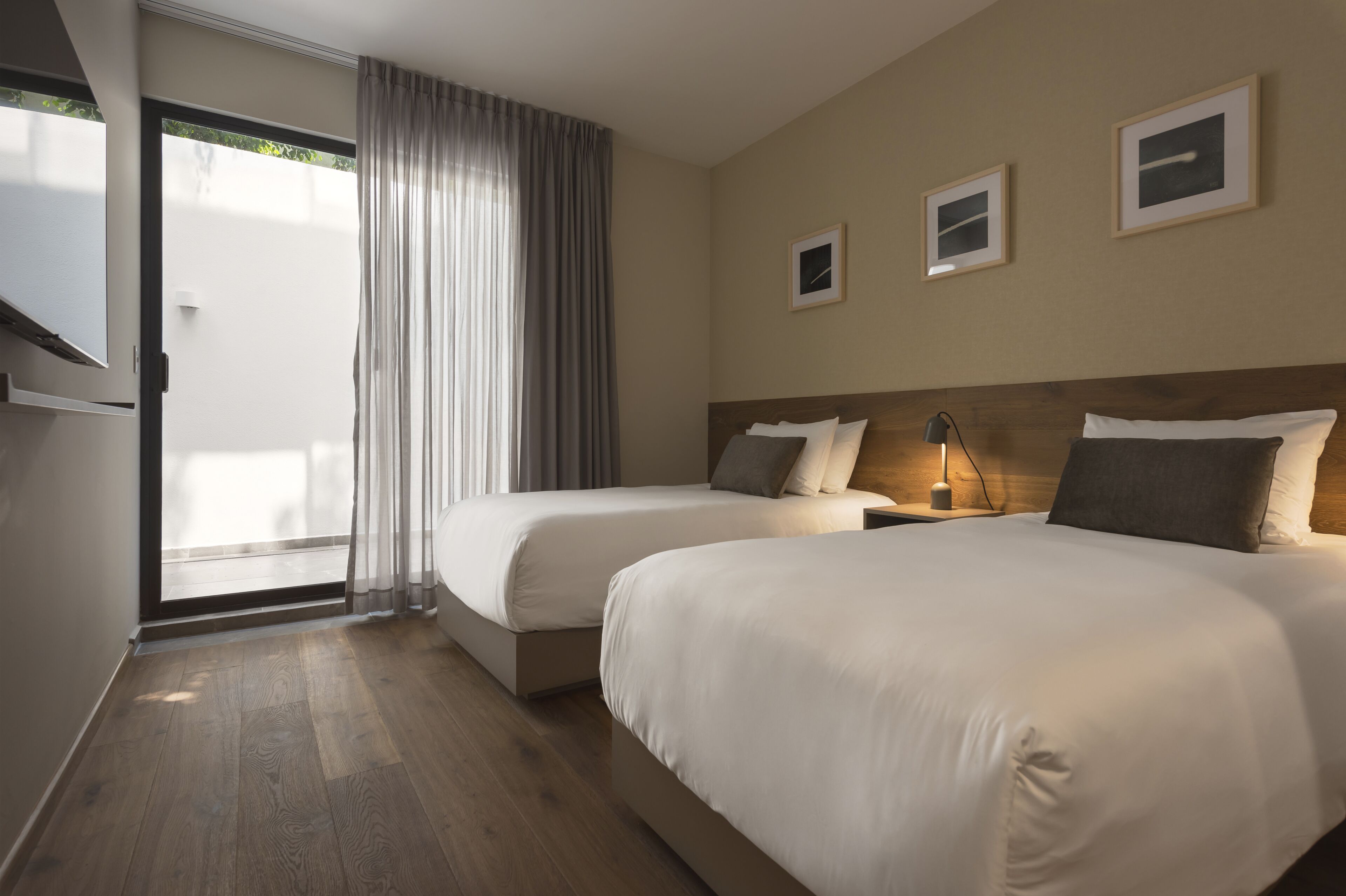 A hotel room with two beds, a sliding glass door to the balcony, and a small table with a lamp.