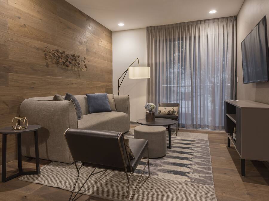 Una sala de estar moderna con sofá, sillón, mesa de centro y televisión.