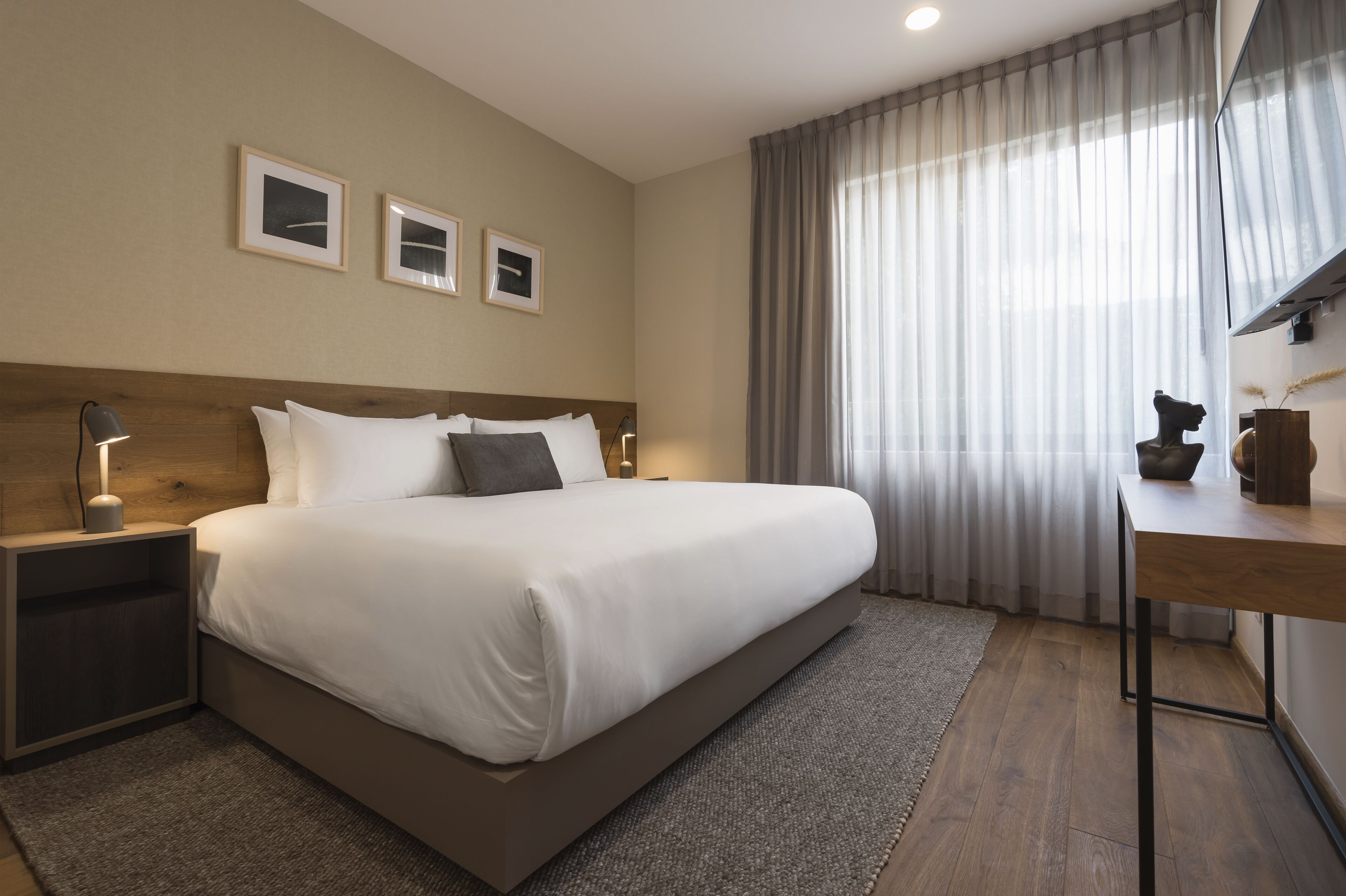 Una habitación de hotel moderna con una cama grande, un escritorio y una ventana con cortinas traslúcidas.