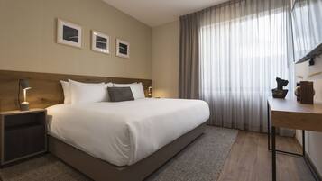 Una habitación de hotel moderna con una cama grande, un escritorio y una ventana con cortinas traslúcidas.