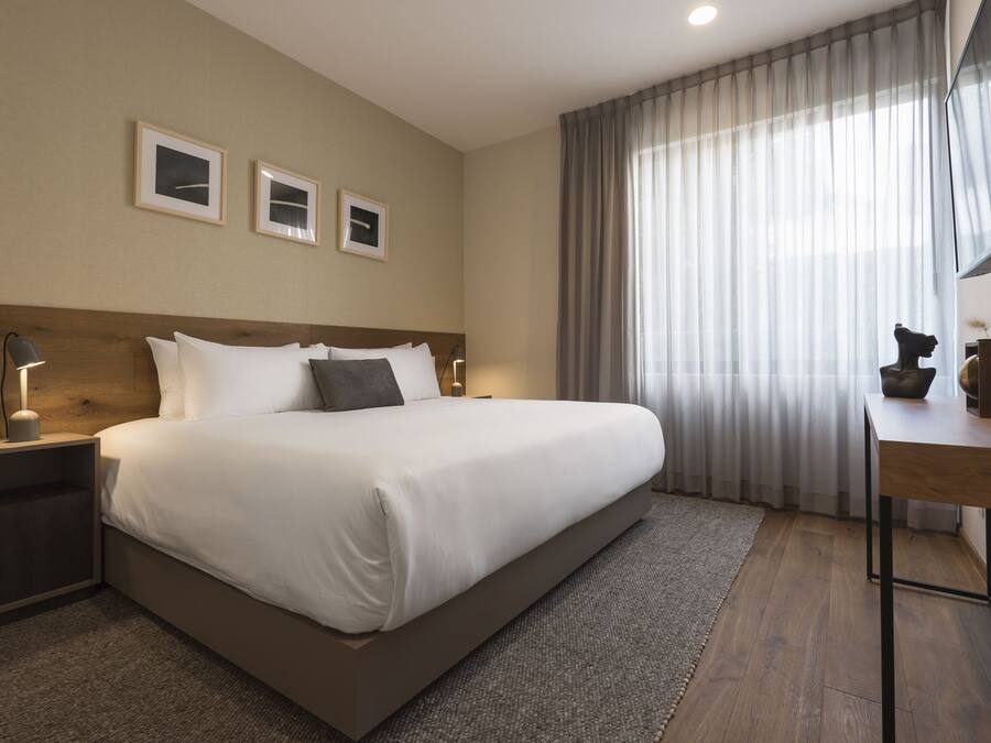 Una habitación de hotel moderna con una cama grande, un escritorio y una ventana con cortinas traslúcidas.