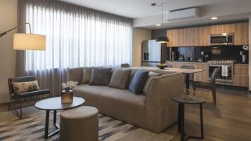 Una sala de estar moderna con sofá, mesa de centro y reposapiés, un comedor con mesa y sillas, y una cocina con electrodomésticos.