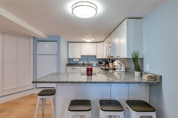 A modern kitchen with white cabinets, a granite countertop, and a central island with stools.