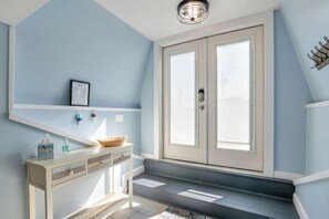 A bathroom with a light blue wall, a white vanity with a basket, a framed certificate, and a door with a handle.