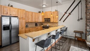 Une cuisine moderne dotée de meubles en bois, d’appareils électroménagers en acier inoxydable et d’un îlot central avec des tabourets de bar.