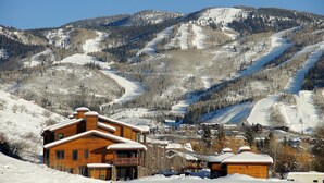 Un chalet en bois doté d’un balcon, entouré de montagnes enneigées et situé à proximité d’une piste de ski.