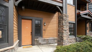 Un bâtiment à l’extérieur en bois, avec un pilier en pierre, une porte et une fenêtre sur laquelle figure un numéro.