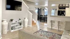 A spacious living room with a ceiling fan, a TV mounted on the wall, and a dining area with a staircase leading to another level. - Great location SixFlags/LaCantera/UTSA/Top Golf (San Antonio)