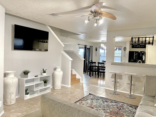 A spacious living room with a ceiling fan, a TV mounted on the wall, and a dining area with a staircase leading to another level. - Great location SixFlags/LaCantera/UTSA/Top Golf (San Antonio)