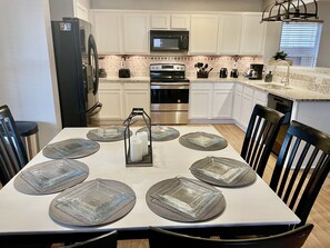 Una cocina moderna con armarios blancos, electrodomésticos de acero inoxidable y una mesa de comedor con posavasos de vidrio y velas.