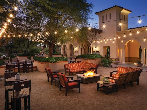 An outdoor patio area with seating, a fire pit, and string lights.