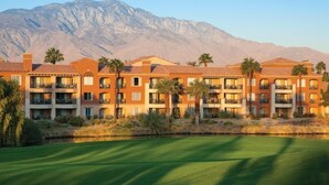 A multi-story hotel with balconies, a pool, and a view of mountains. - Coachella 2023 (Palm Desert)