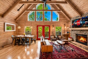 A log cabin interior with a dining area, seating, a fireplace, and a TV.