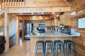 A wooden cabin interior with a kitchen featuring a large island, bar stools, and a refrigerator.