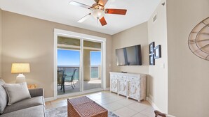 A living room with a sofa, a coffee table, a TV, and a balcony with a view. - Grand Panama 1003 - Pets OK, Gulf Front, Huge Balcony, Sleeps 8 (Panama City Beach)