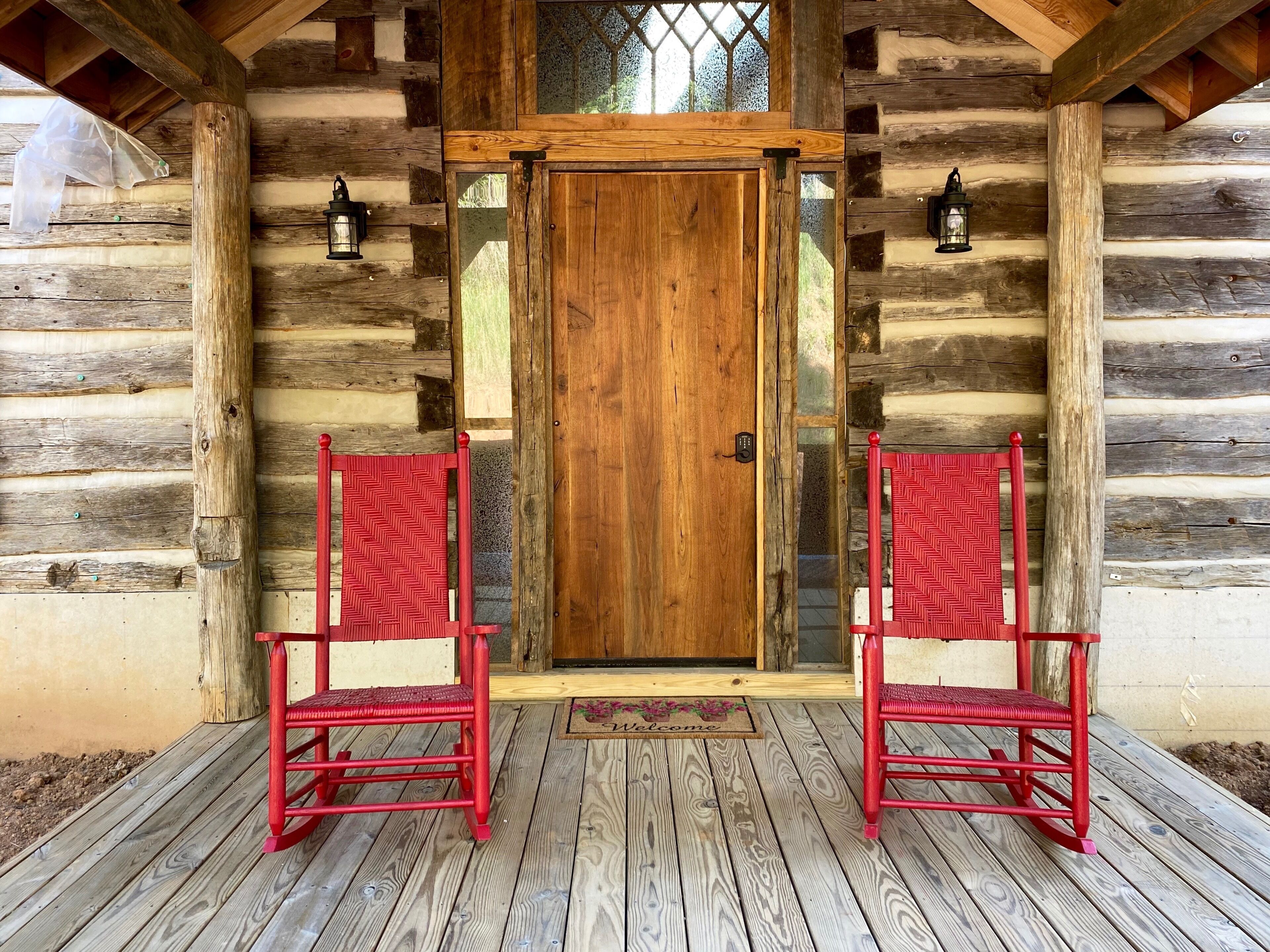 L’entrée d’un chalet en bois, avec une porte en bois et deux chaises rouges sur une terrasse en bois.