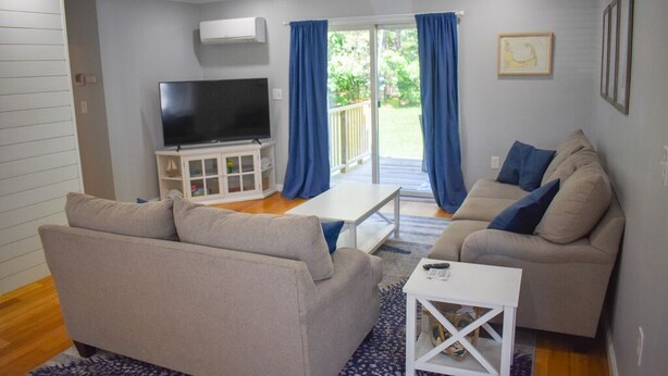 A living room with two sofas, a TV, and a sliding glass door to a balcony. - Pristine condition! Three bedroom sleeping 8 with contemporary beach decor! (South Dennis)