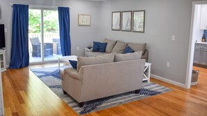 A modern living room with a sofa, a coffee table, and a TV. There is a sliding glass door leading to an outdoor area. - Pristine condition! Three bedroom sleeping 8 with contemporary beach decor! (South Dennis)