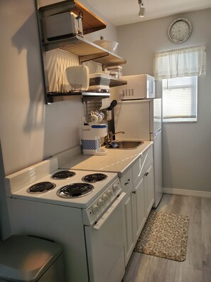A compact kitchen with a stove, microwave, and a clock on the wall.