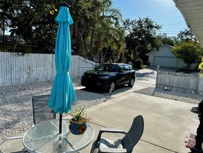 A residential driveway with a parked car, a patio table with a potted plant, and a blue umbrella.