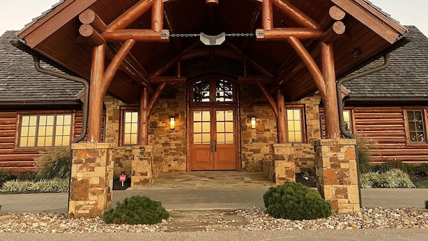 Un bâtiment de style « cabane en rondins », doté d’une entrée imposante, de fondations en pierre et d’un porche abrité.