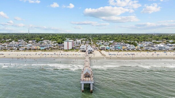 Une jetée qui s’avance dans l’océan, avec une plage et des immeubles résidentiels en arrière-plan.