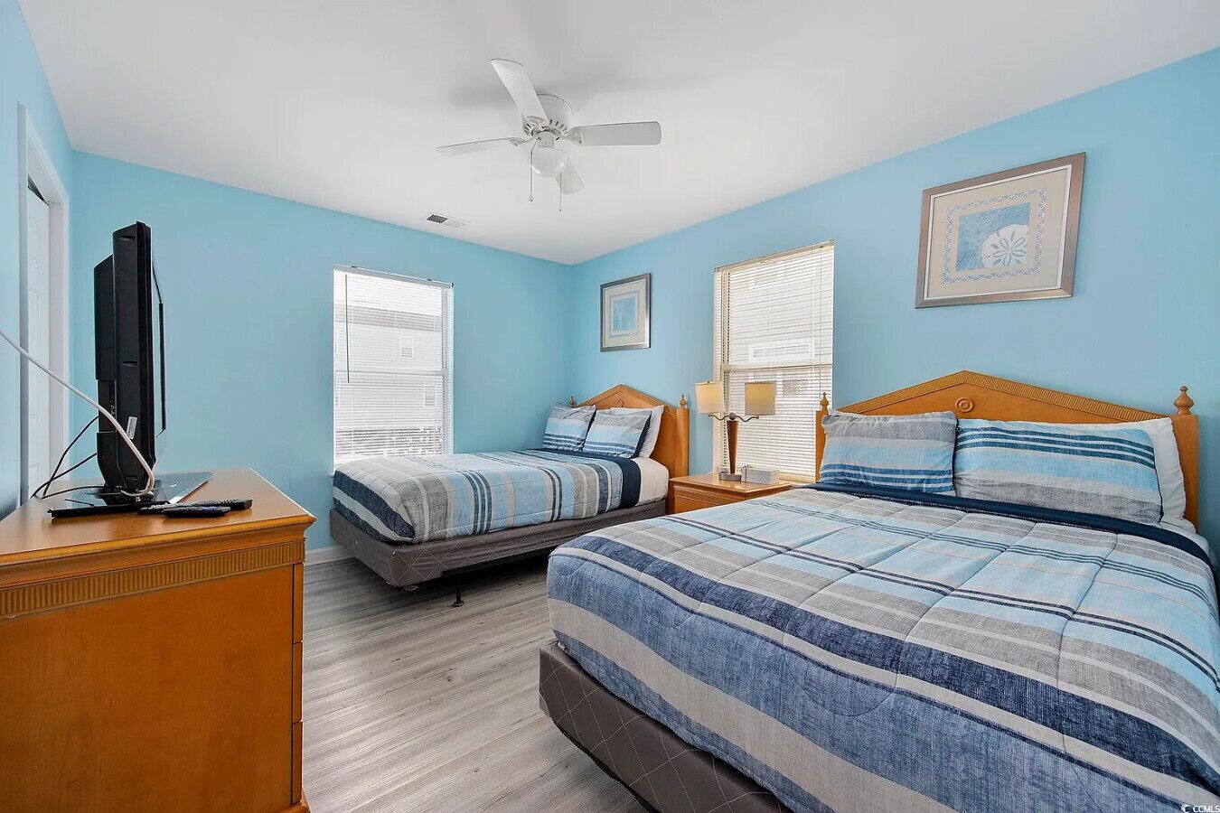 A bedroom with two beds, a ceiling fan, and a television on a wooden dresser.