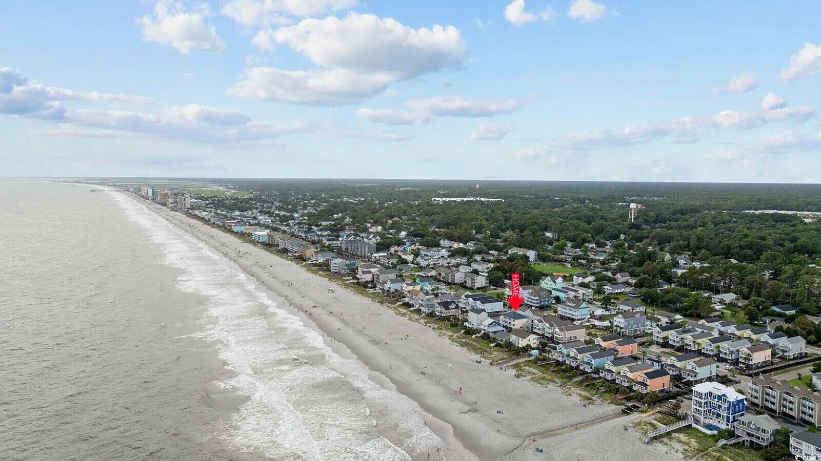 A coastal residential area with houses along the beach, a clear sky, and a distant view of the ocean.