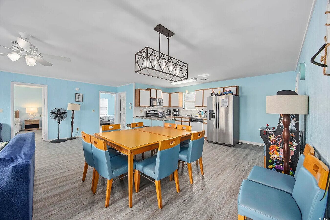A modern kitchen with stainless steel appliances, a dining area with blue chairs, and a ceiling fan.