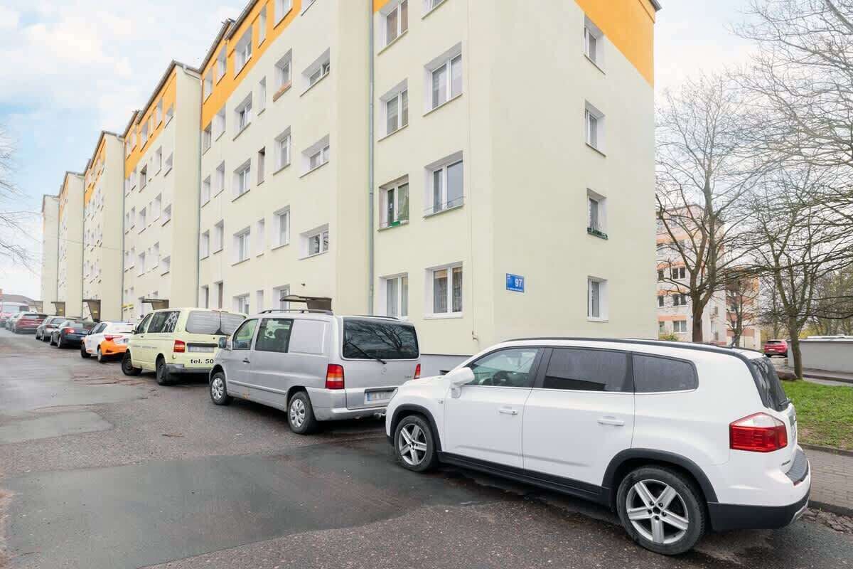 Une rangée de voitures garées devant un immeuble résidentiel à plusieurs étages, dont la façade est jaune et blanche.