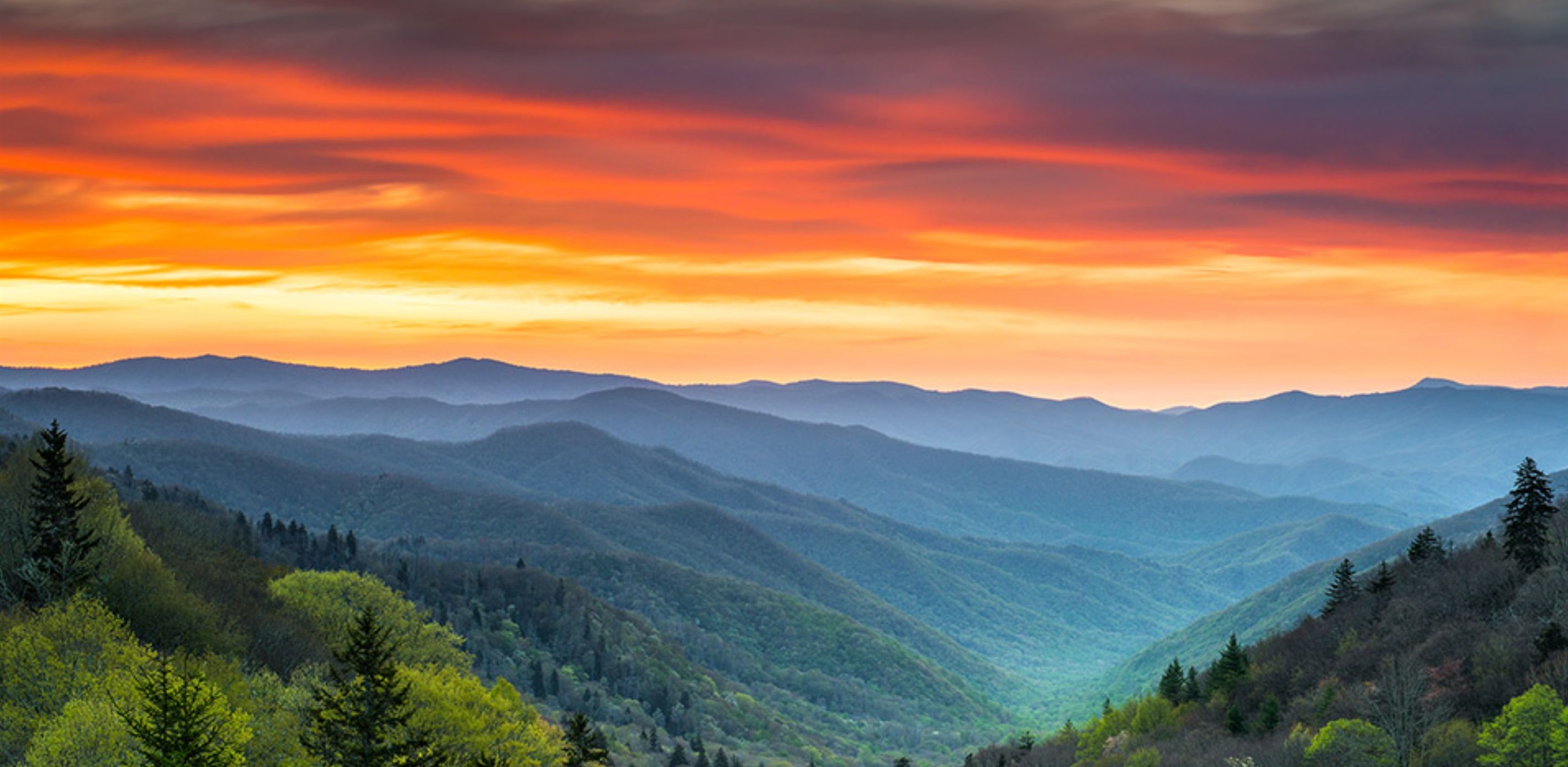 A mountainous landscape with a valley and forested hills.