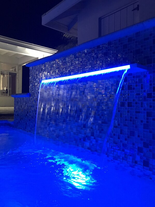 A nighttime view of a swimming pool with a waterfall feature and blue lighting.