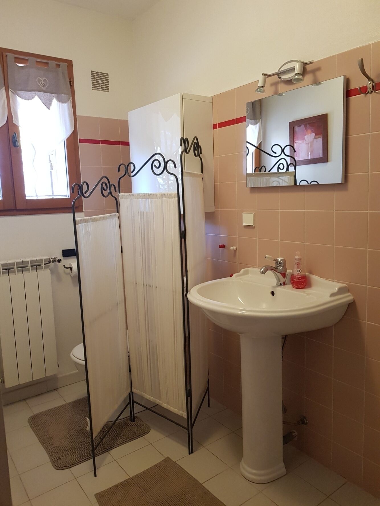 Ein Badezimmer mit einem weißen Waschbecken, einem Spiegel, einer Heizung und einer Duschkabine.