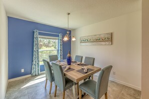 A dining area with a wooden table, six chairs, a vase, and a painting on the wall.