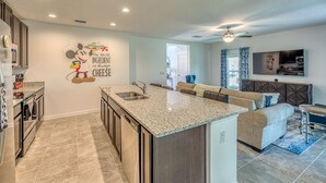 A modern kitchen with a granite island, built-in appliances, and a Mickey Mouse wall decal. - Brand New, Stylish 4-Bed 3-Bath Home. Conservation Views & Gated Resort Amenities. Near Disney! (Davenport)