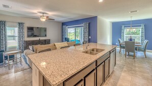 A modern kitchen with granite countertops, a central island, and a dining area with blue chairs. - Brand New, Stylish 4-Bed 3-Bath Home. Conservation Views & Gated Resort Amenities. Near Disney! (Davenport)