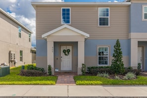 A two-story residential building with a front entrance, a mailbox, and a wreath on the door.